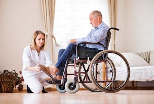Visitatore sanitario o un infermiere e un uomo anziano su una sedia a rotelle durante la visita domiciliare. Un'infermiera che aiuta un uomo anziano a mettersi una pantofola.