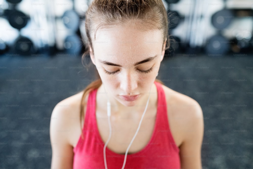 Beautiful young fit woman in gym resting, earphones in her ears, listening music