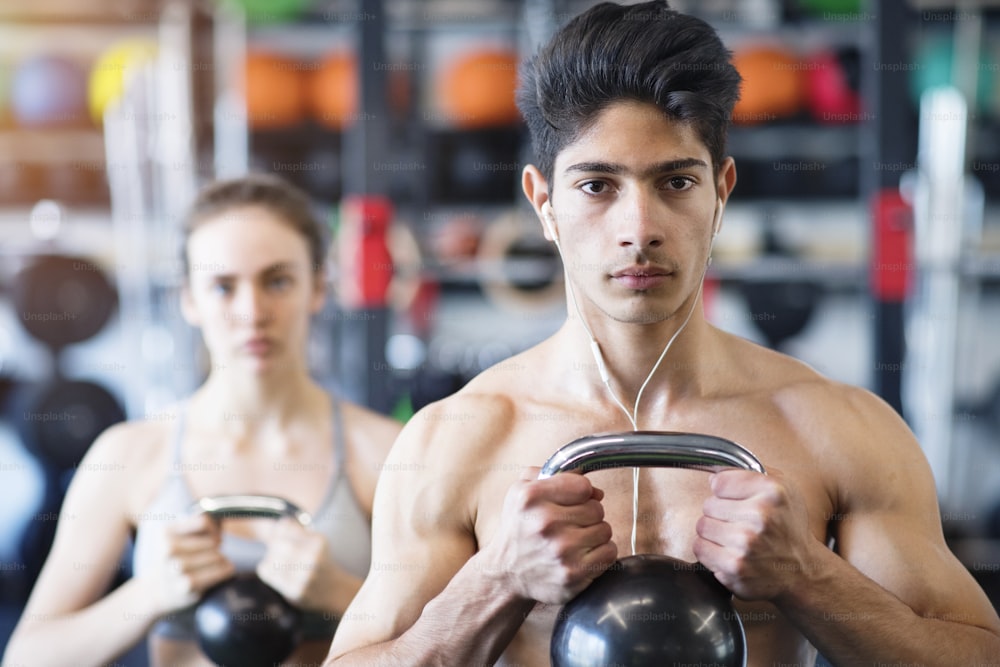 Beautiful young fit couple doing strength training, exercising with kettlebell in modern gym.