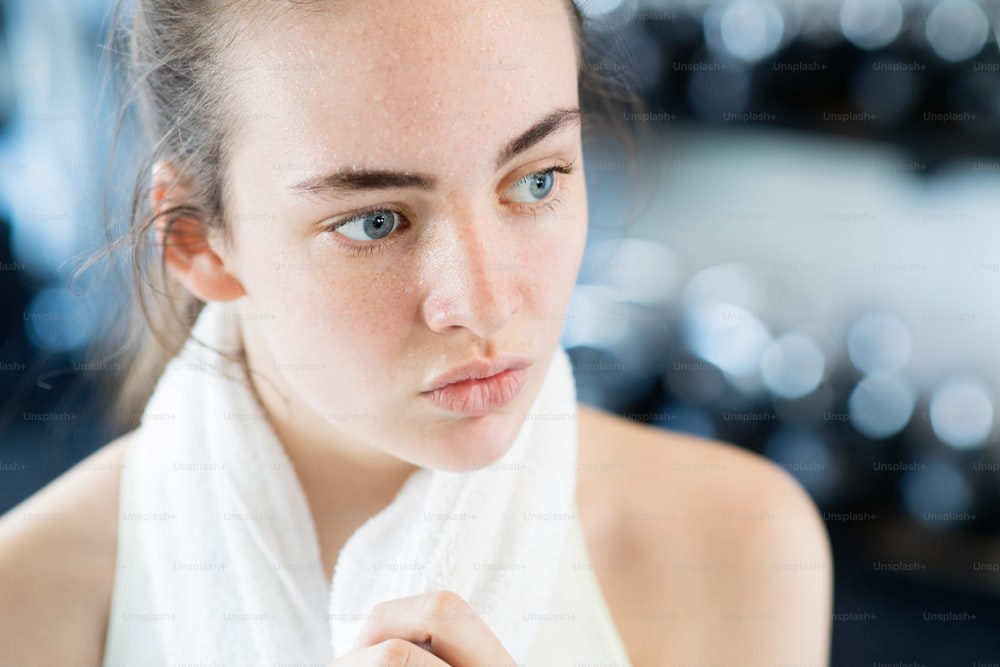 Face of beautiful young fit woman in gym towel around her neck, resting