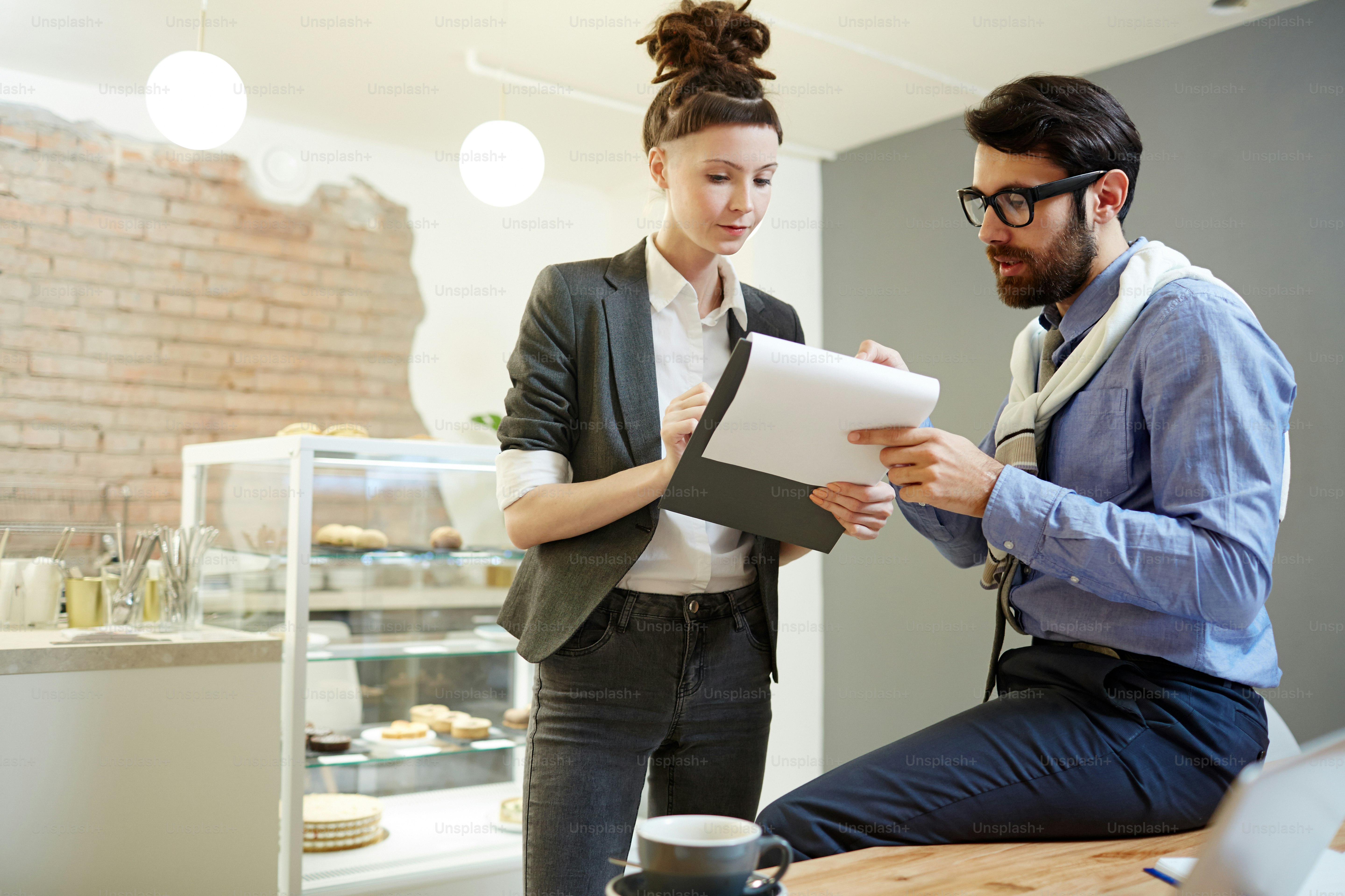Young elegant businesswoman pointing at business document while explaining it to colleague