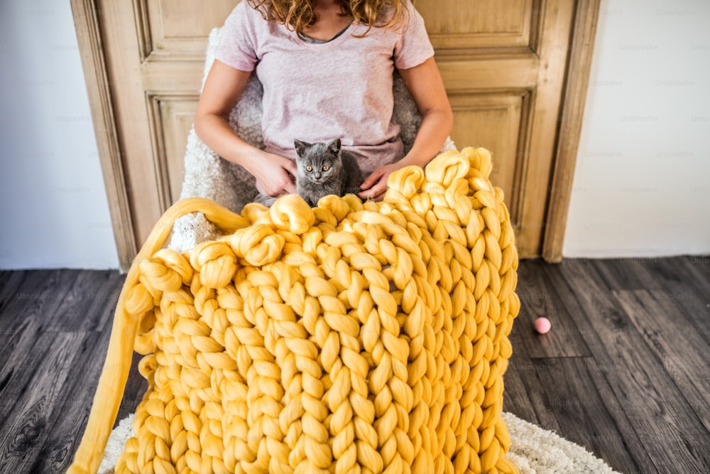 젊은 여성의 중소기업. 모직 담요를 손으로 뜨개질하는 새끼 고양이를 가진 알아볼 수 없는 젊은 여성.