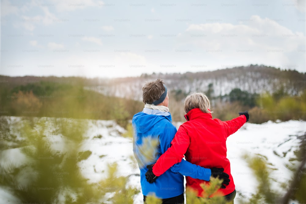 Couple de personnes âgées faisant du jogging à l’extérieur dans la nature hivernale, se reposant. Vue arrière.