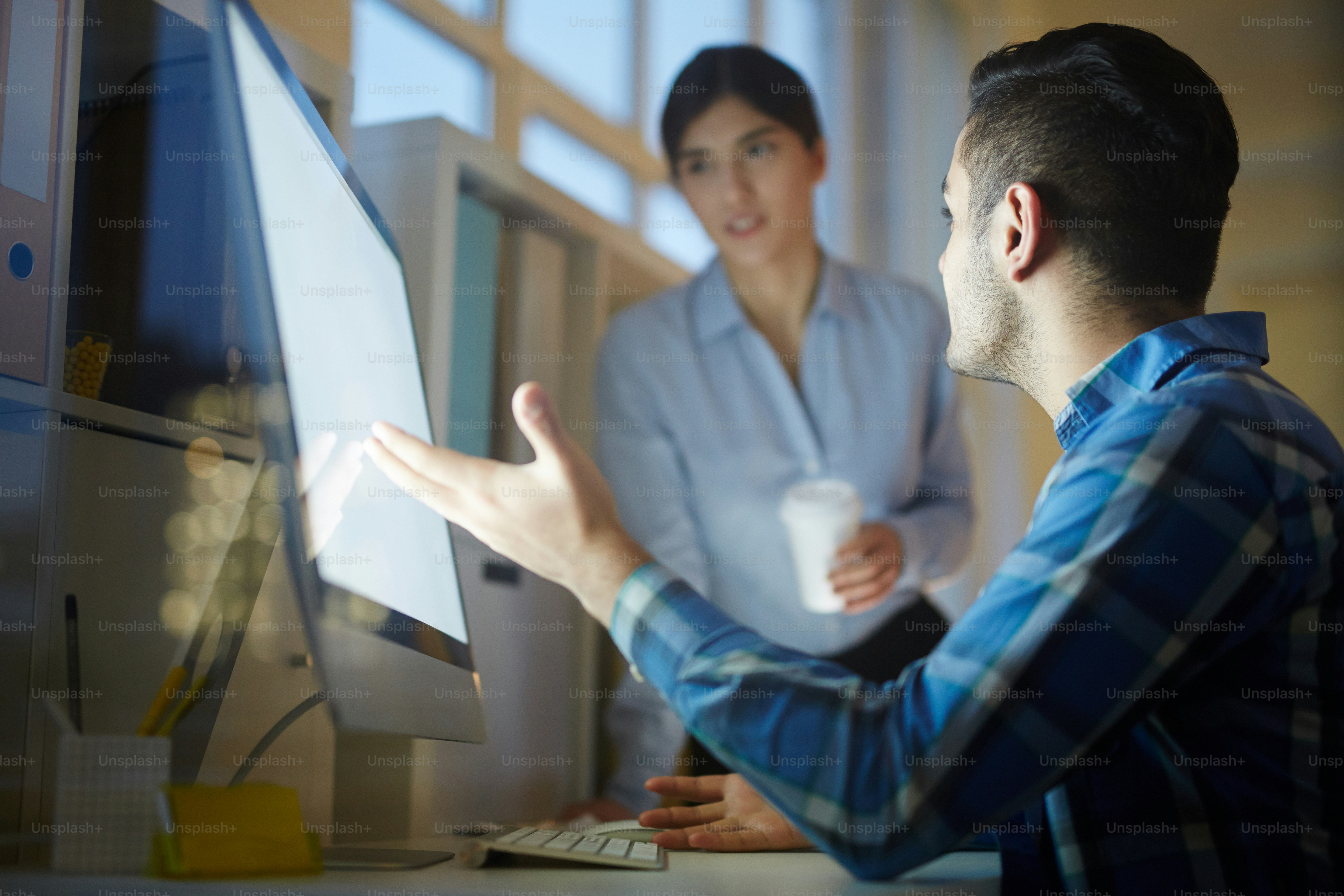 Young man showing his colleague online data in computer during discussion of their ideas