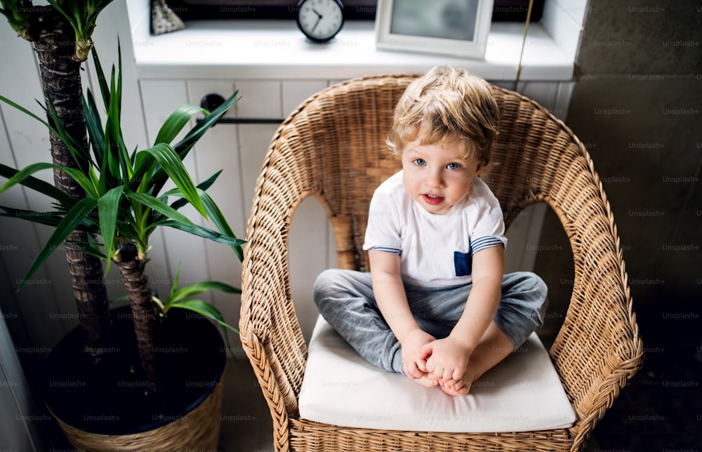 A portrait of a toddler boy sitting on the wicker chair in the bathroom at home.
