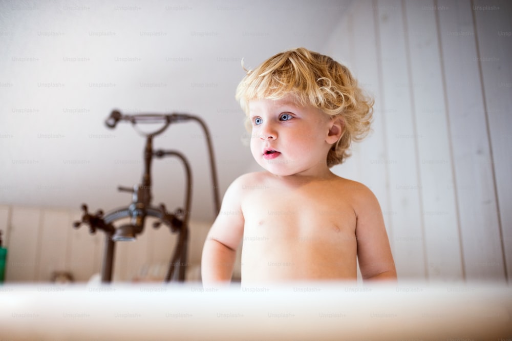 Mignon petit garçon en bas âge debout dans la baignoire de la salle de bain.