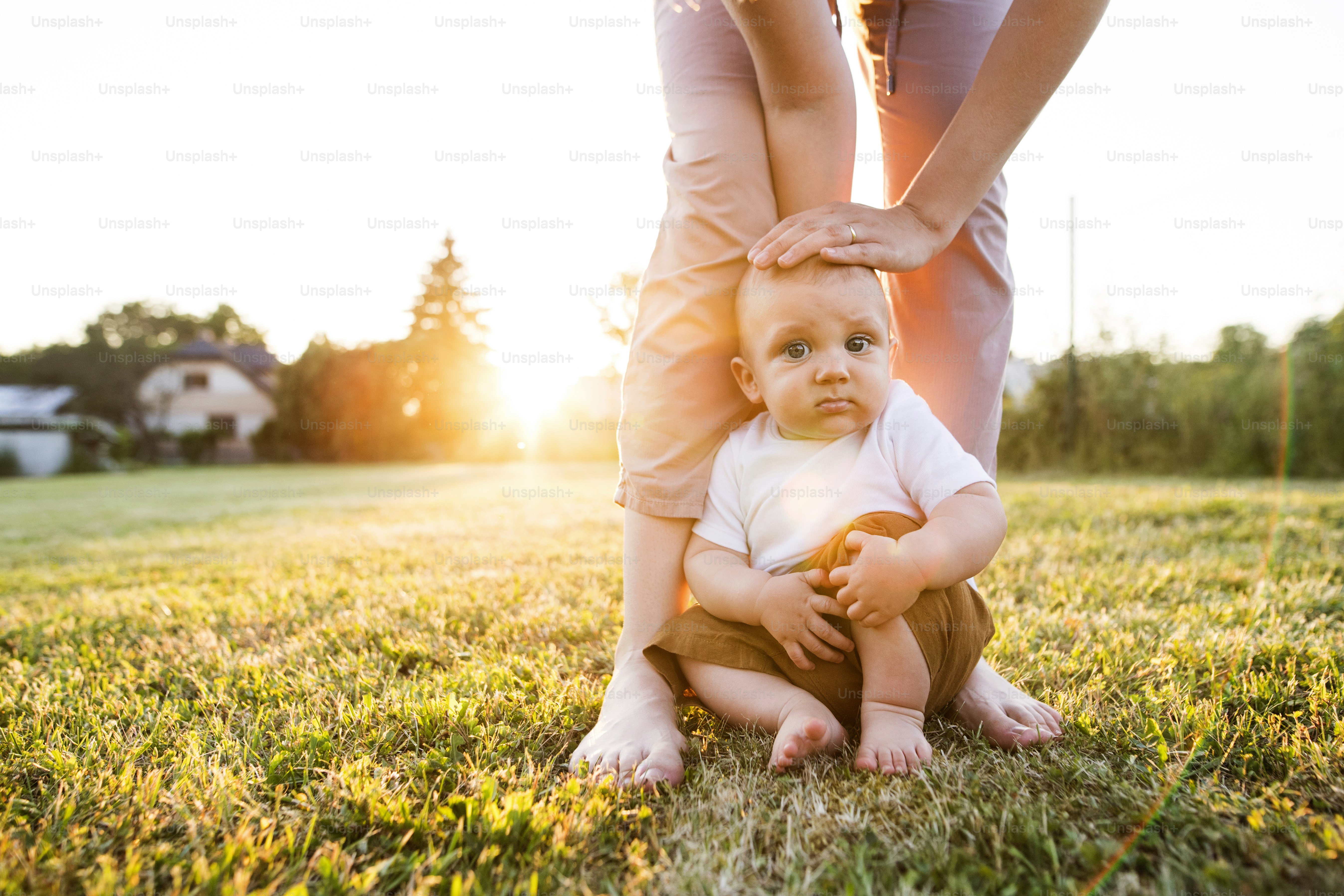 Cute baby boy with his unrecognizable mother outside in the garden.