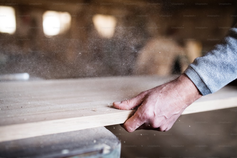 A hand of an unrecognizable man worker in the carpentry workshop, working with wood.