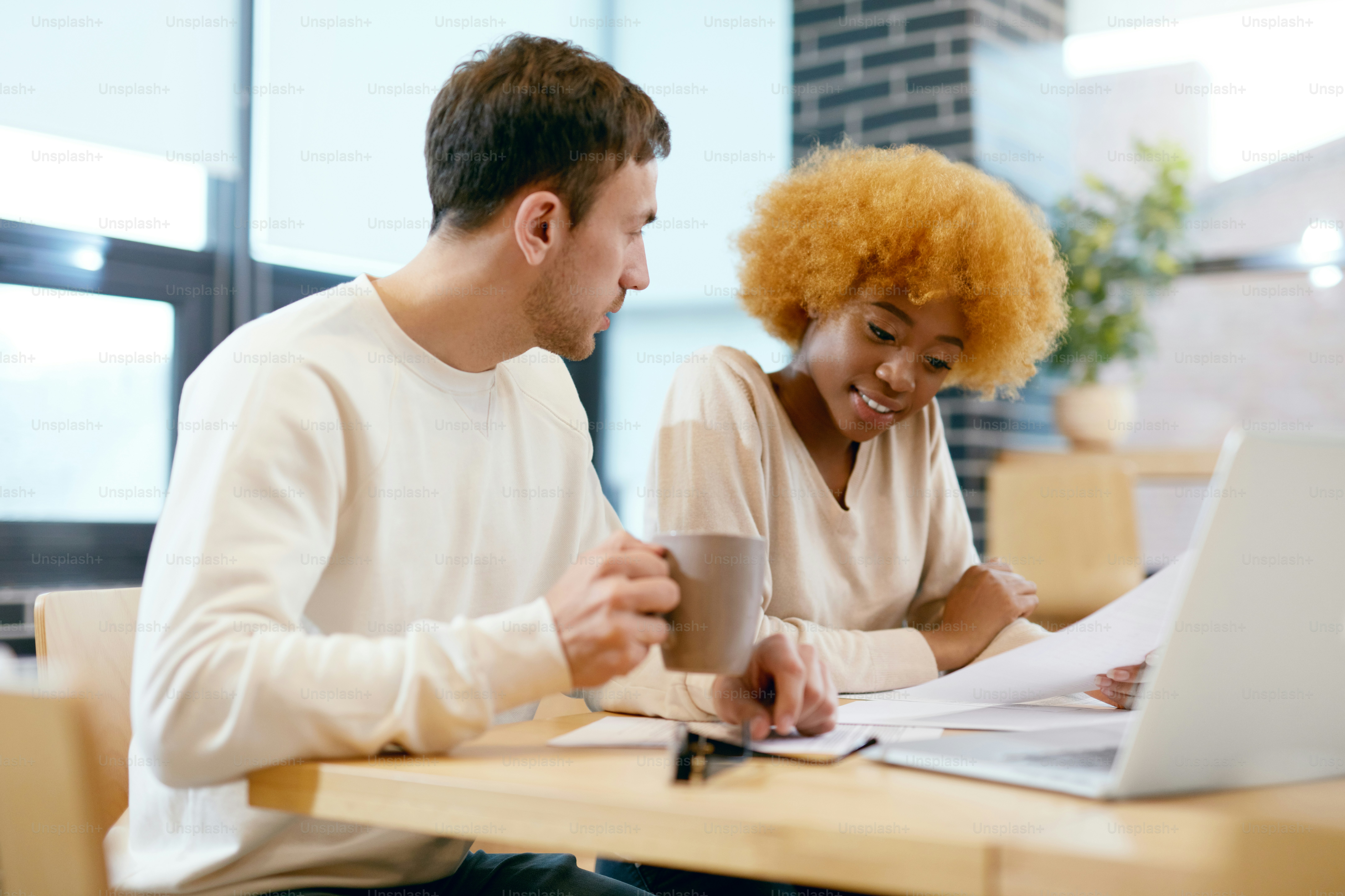 People Working On Notebook In Cafe. Smiling Young Man And Beautiful Black Woman Working Together On Project, Using Computer And Sharing Ideas In Coffee Shop. Business Team At Work. High Quality