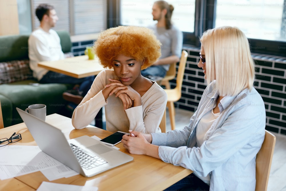 Business Women Working In Cafe. Beautiful Happy Young Female Co-workers Sitting At Table With Notebook And Working Together On Project. Teamwork. High Quality Image