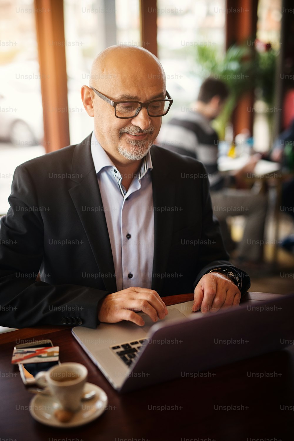 成熟した幸せなビジネスマンは、コーヒーショップに座っている間、ラップトップで見たものに満足しています。