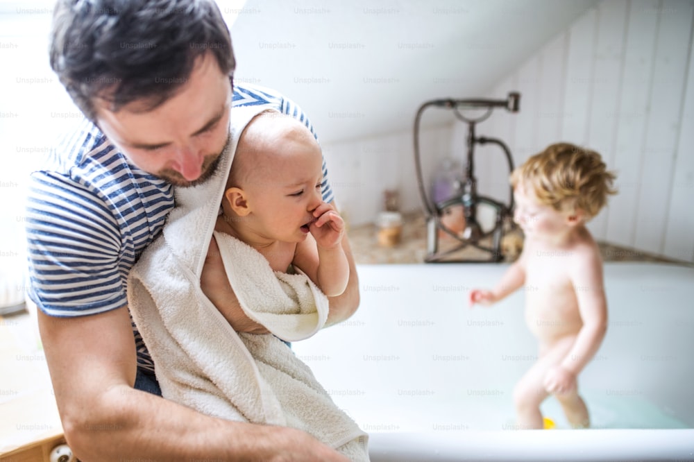 Vater wäscht zwei Kleinkinder in der Badewanne im Badezimmer zu Hause. Vaterschaftsurlaub.
