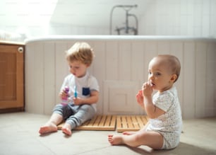 Zwei Kleinkinder sitzen zu Hause auf dem Boden und putzen die Zähne im Badezimmer.