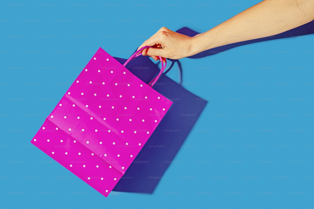 una mano che tiene una borsa della spesa rosa su sfondo blu