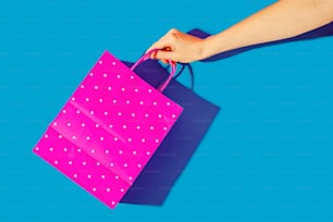 a hand holding a pink shopping bag on a blue background