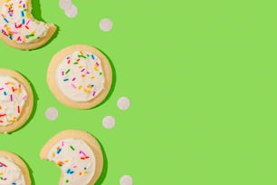 three cookies with white frosting and sprinkles on a green background