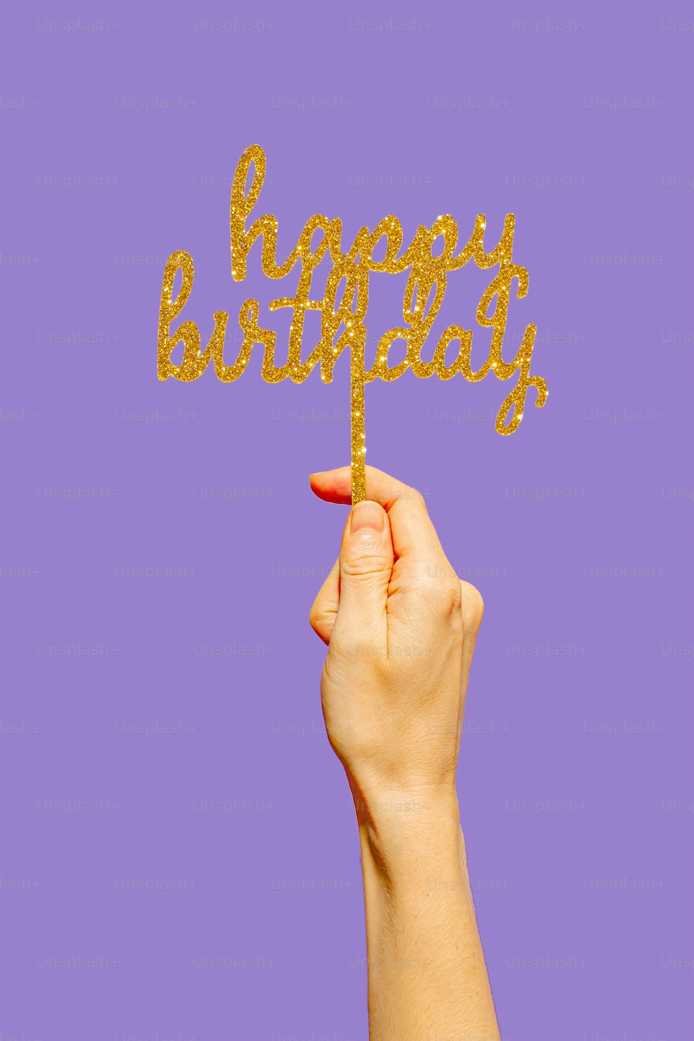 a hand holding a gold happy birthday cake topper