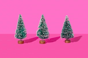 three small christmas trees on a pink background