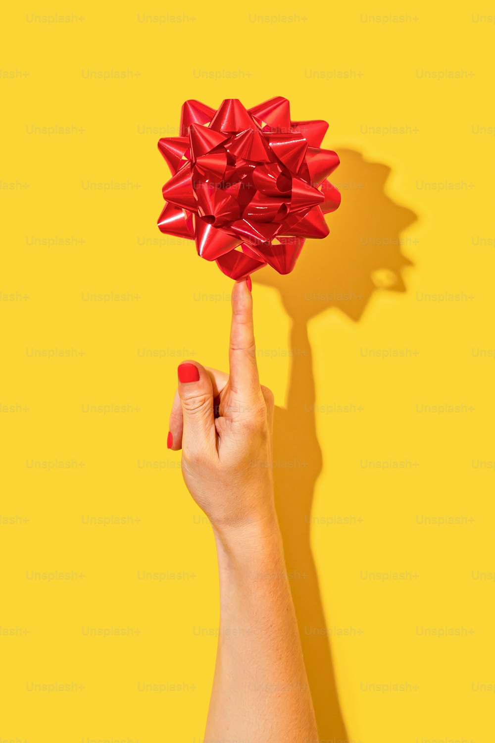 a woman's hand holding a red bow on a yellow background