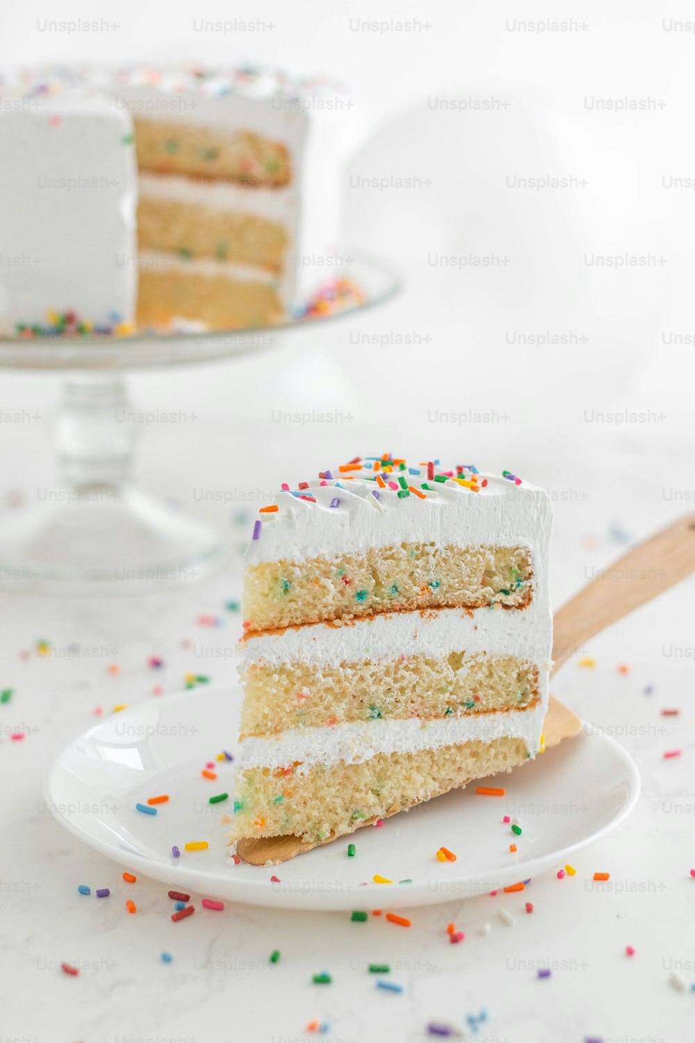 a slice of cake with white frosting and sprinkles on a plate