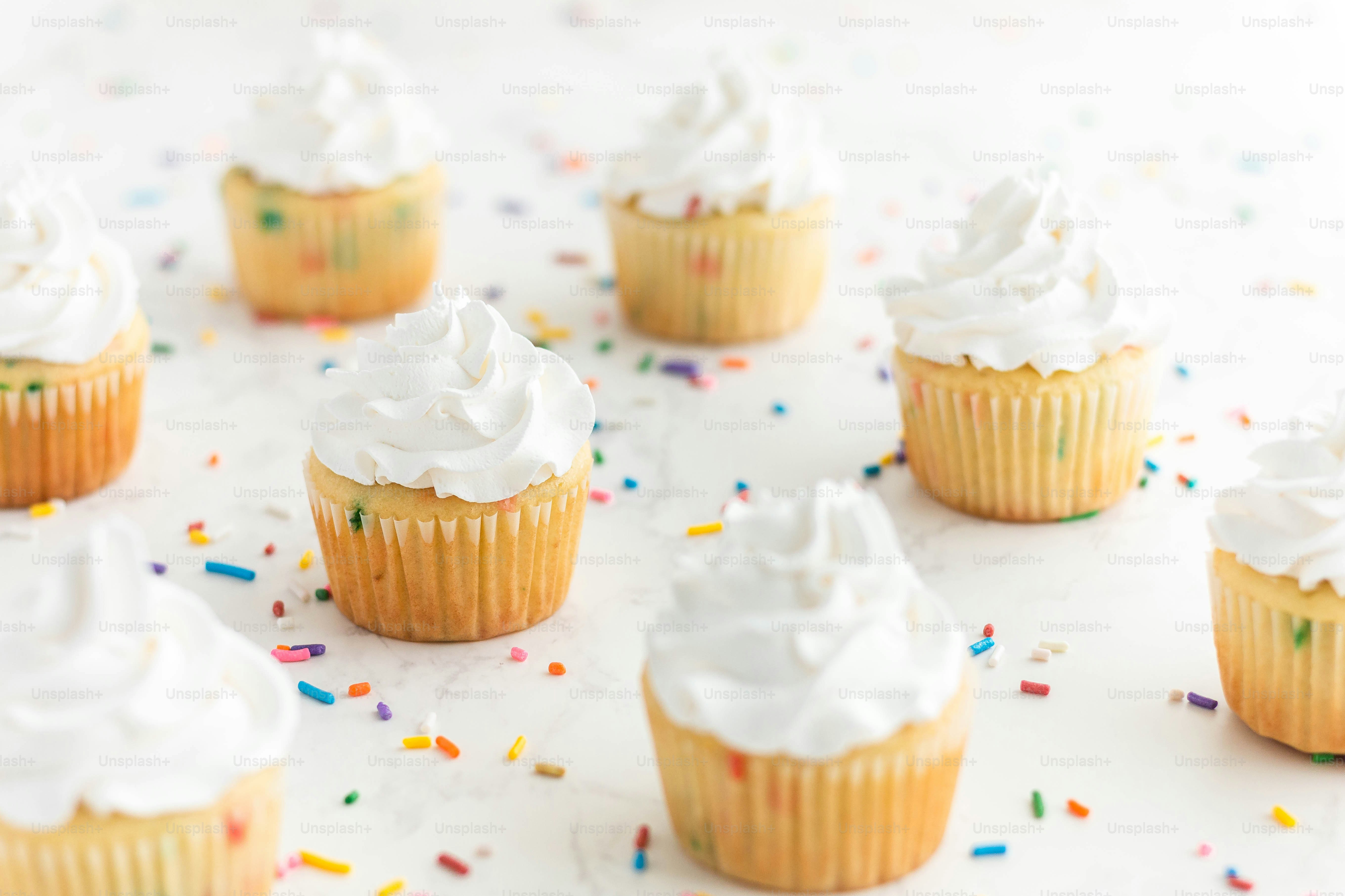 a bunch of cupcakes with white frosting and sprinkles