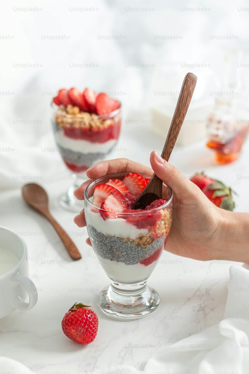 a person holding a spoon over a dessert in a glass