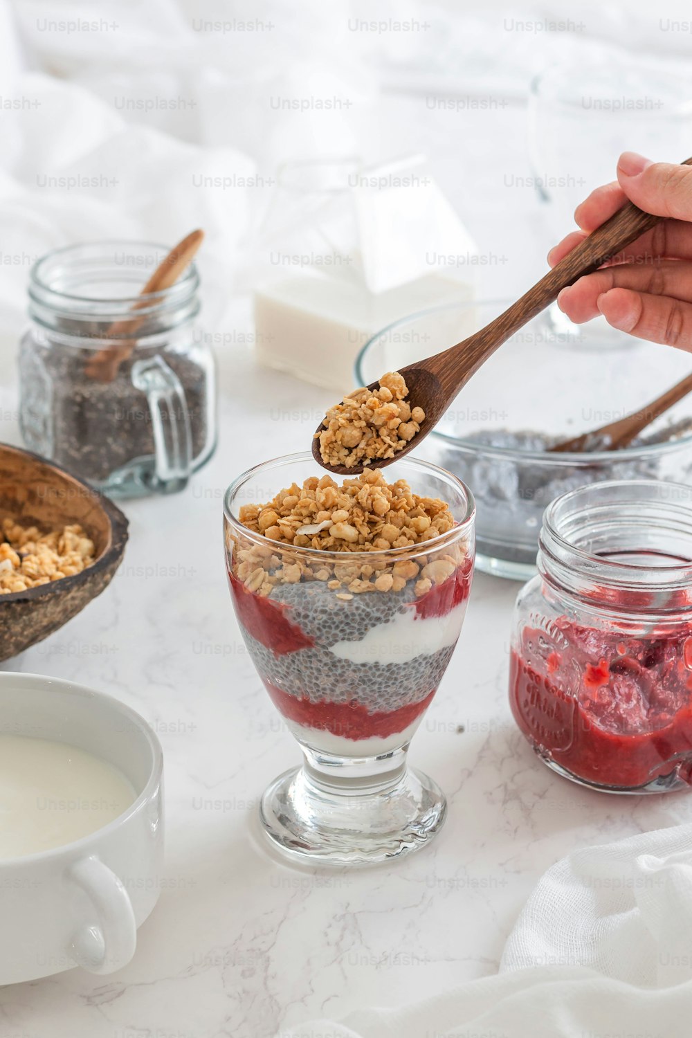 a person spoons a spoonful of granola into a glass