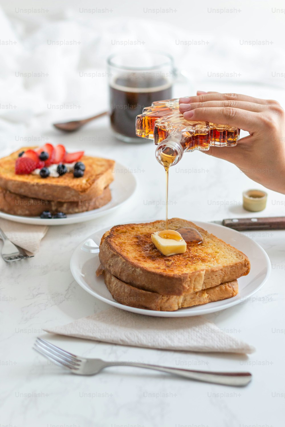 a person pouring syrup on a plate of french toast