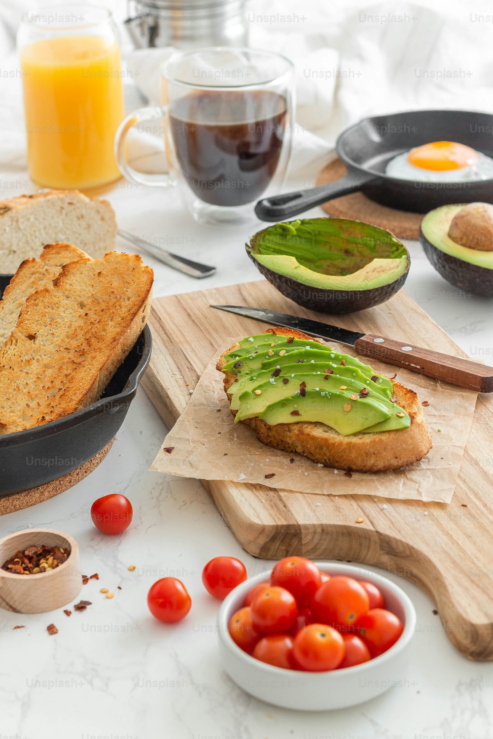 a table topped with bread, tomatoes, avocado and other foods