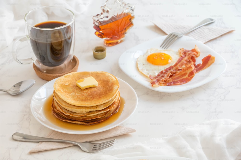 a table topped with pancakes and bacon next to a cup of coffee