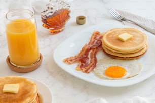 un piatto bianco condito con pancake e pancetta accanto a un bicchiere di succo d'arancia