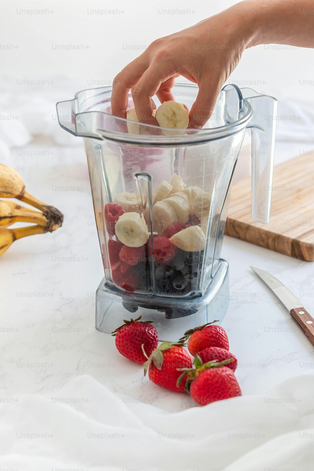 a person is putting bananas and strawberries in a blender