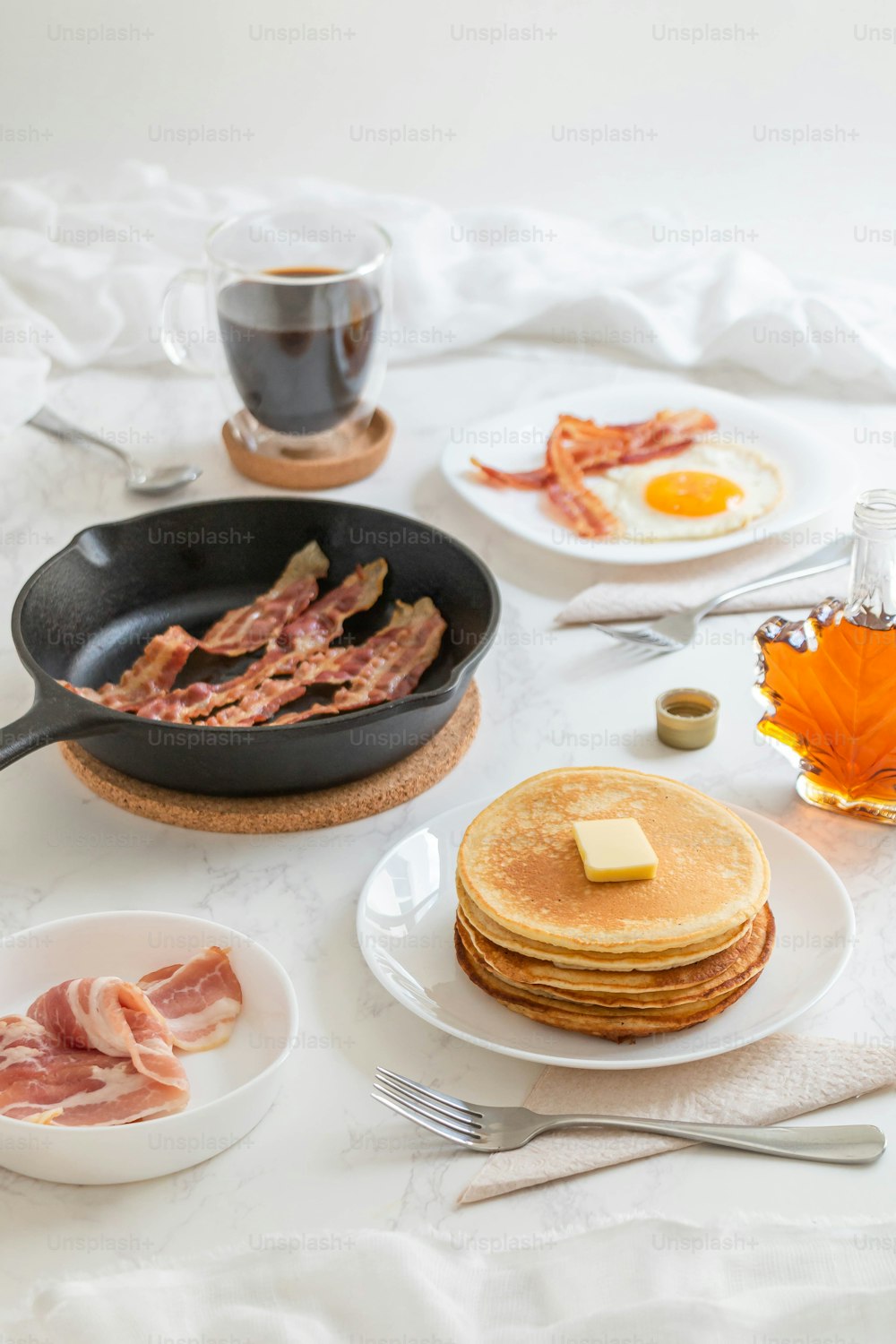 a table topped with pancakes and bacon next to a cup of tea