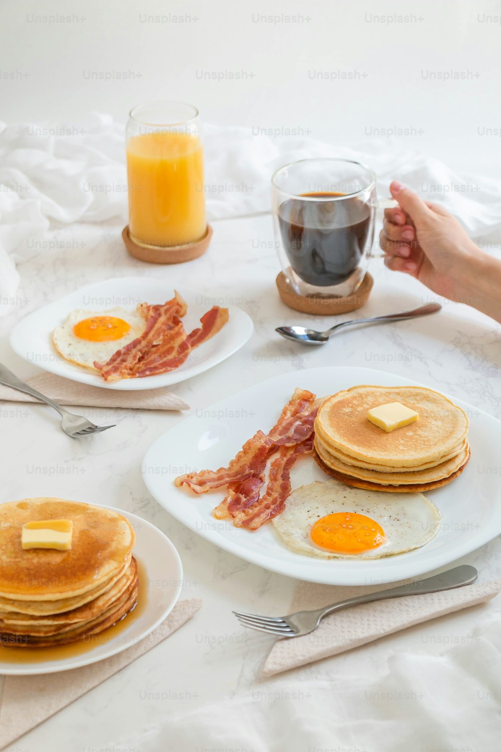 a table topped with pancakes and bacon next to a glass of orange juice