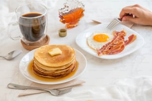 uma mesa com panquecas, bacon, ovos e uma xícara de café