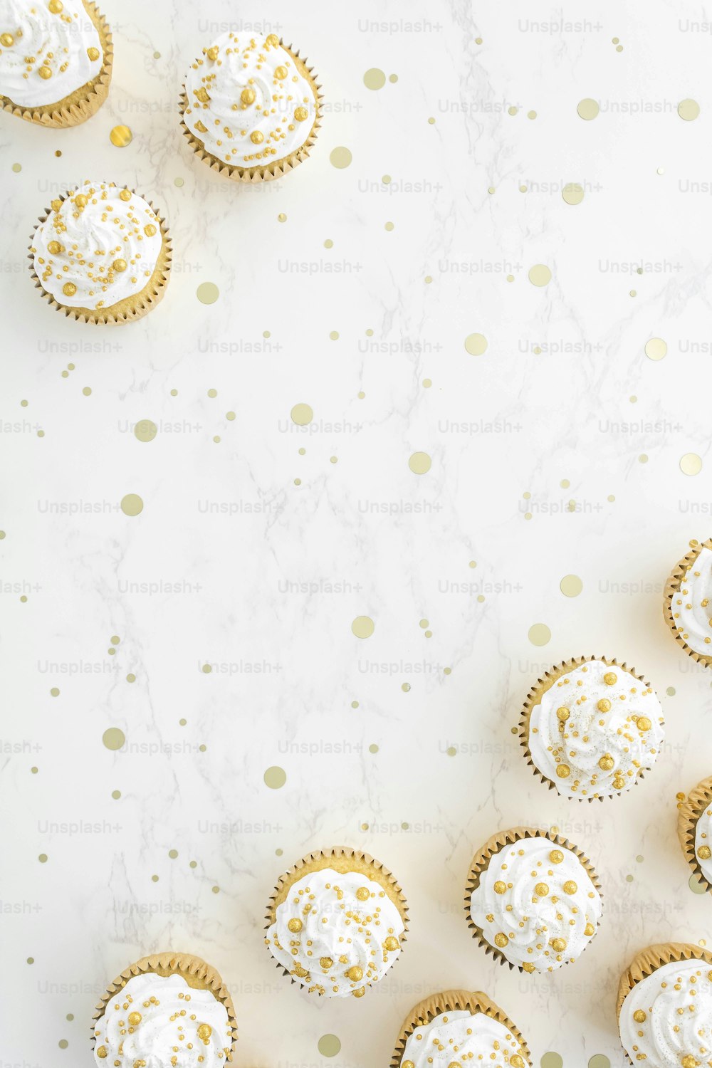 cupcakes with white frosting and gold sprinkles on a white