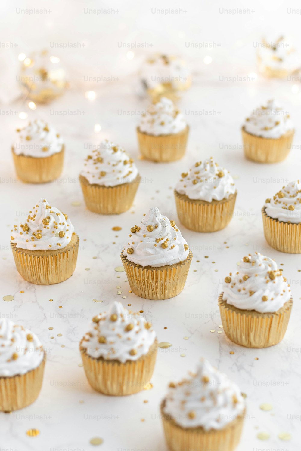 a bunch of cupcakes with white frosting and gold sprinkles