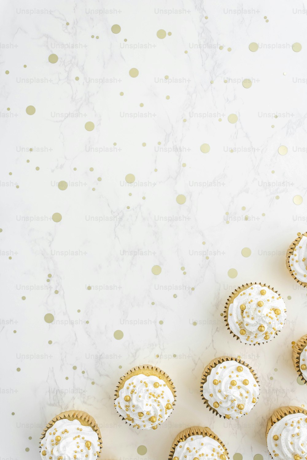 cupcakes with white frosting and gold sprinkles on a marble