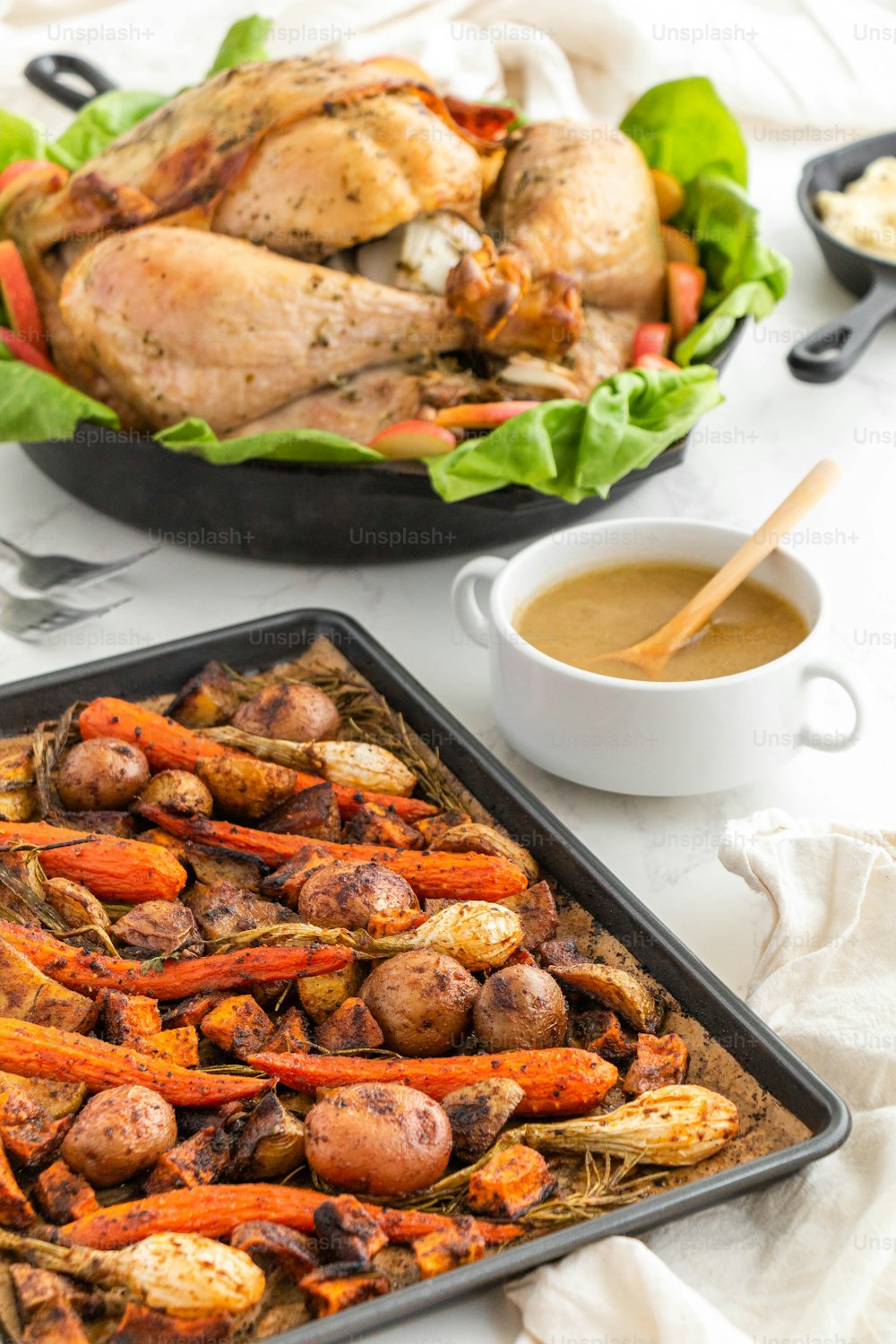a tray of roasted carrots next to a roasting pan of chicken