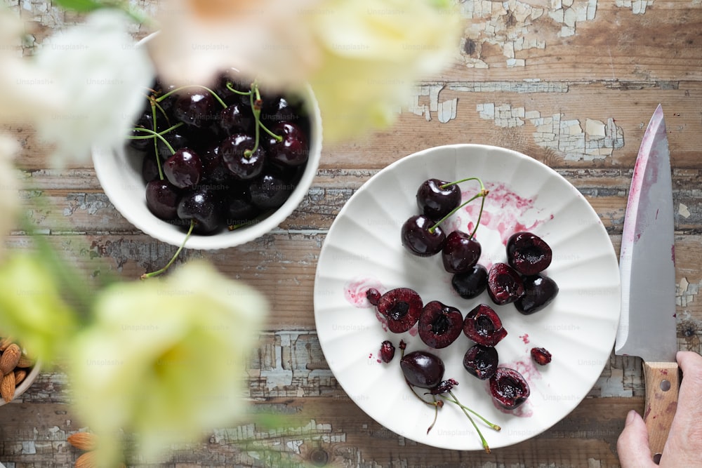 a white plate topped with cherries next to a bowl of cherries