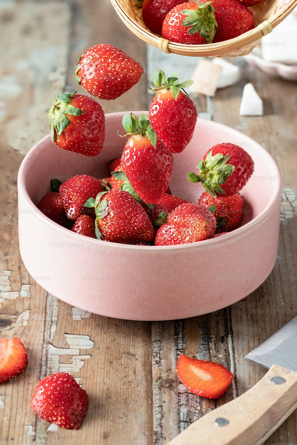 a pink bowl filled with strawberries on top of a wooden table