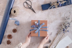 eine Person, die eine verpackte Geschenkbox mit einem blauen Band in der Hand hält