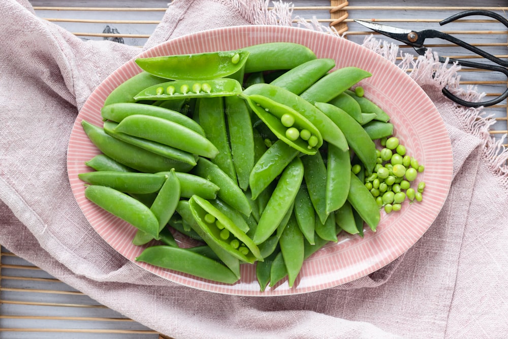a pink plate filled with green beans and peas