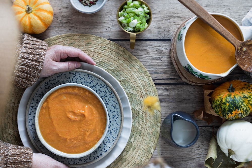 a person holding a bowl of soup on top of a wooden table