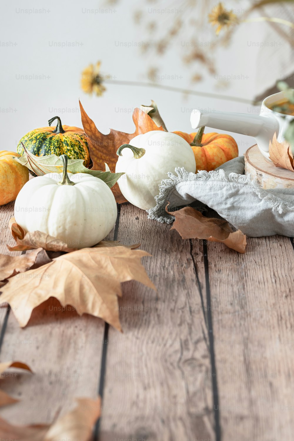 a wooden table topped with white pumpkins and leaves