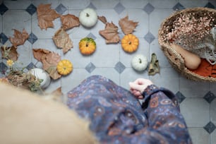a person sitting on a tiled floor next to a basket of pumpkins