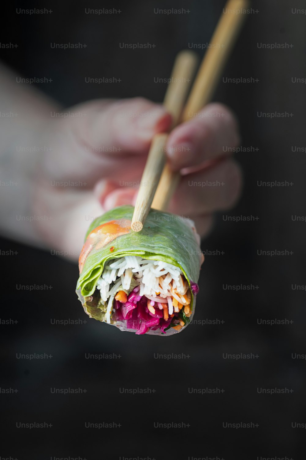 a person holding a sushi roll with chopsticks