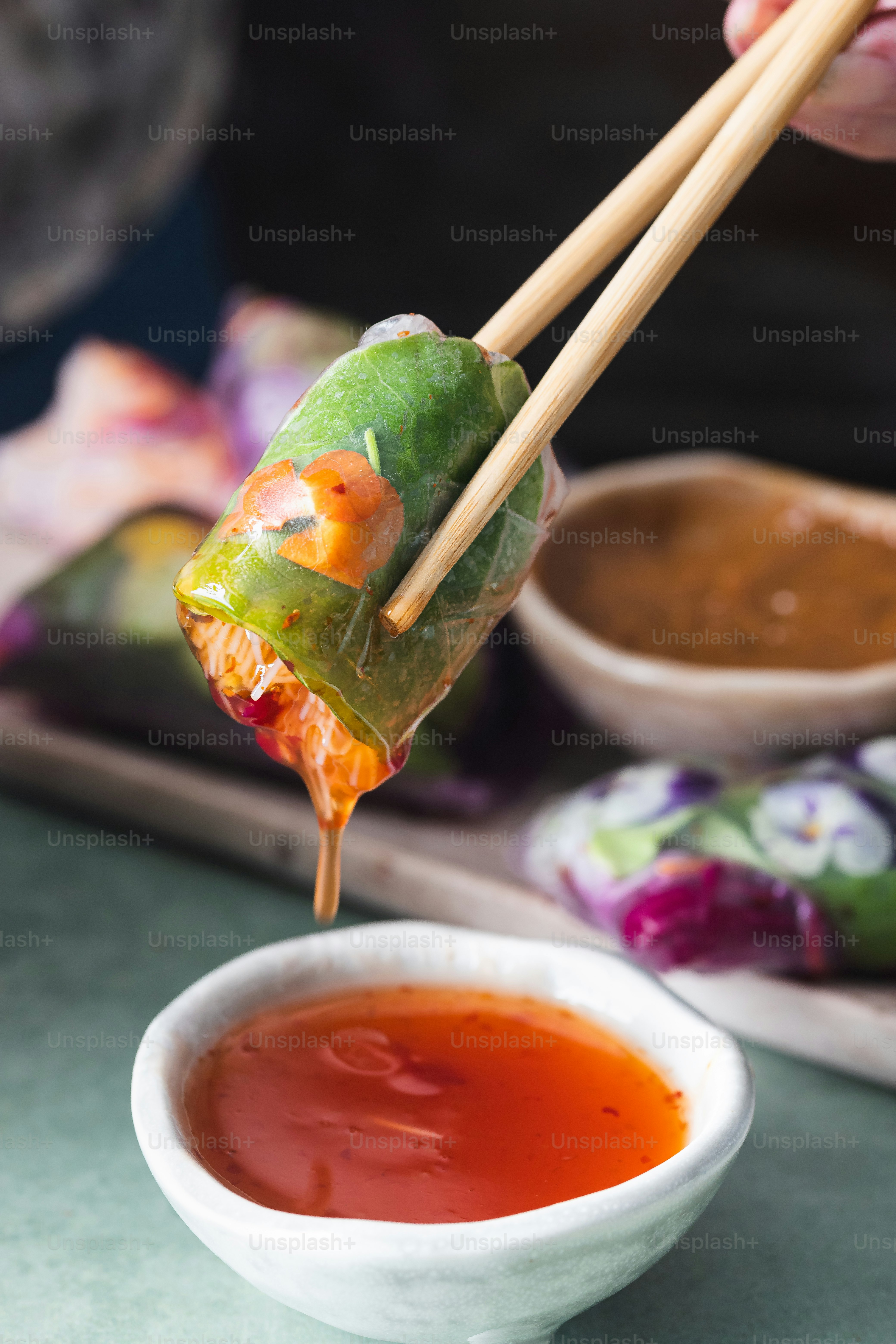 a person holding chopsticks over a bowl of dipping sauce
