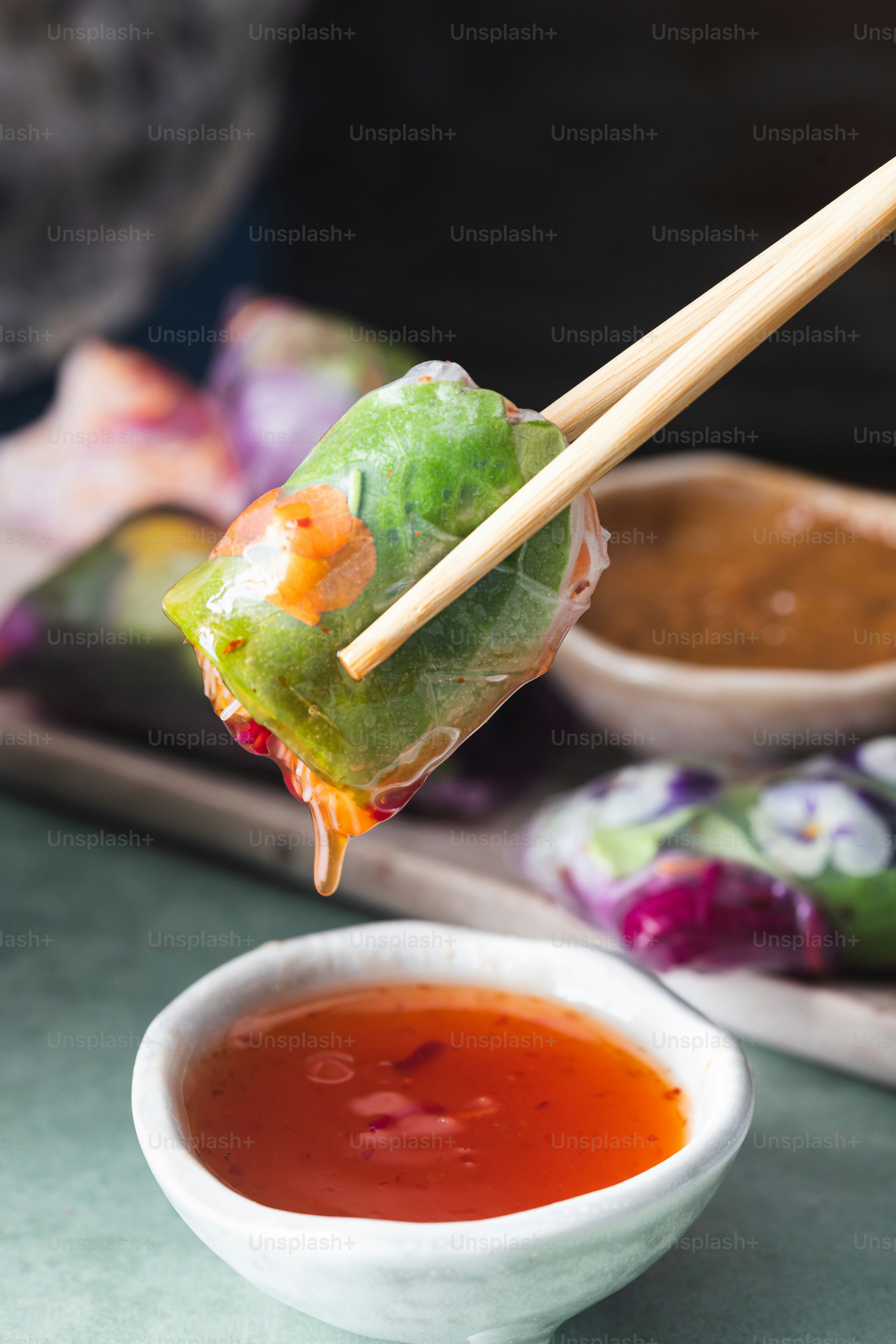 a person holding chopsticks over a bowl of dipping sauce