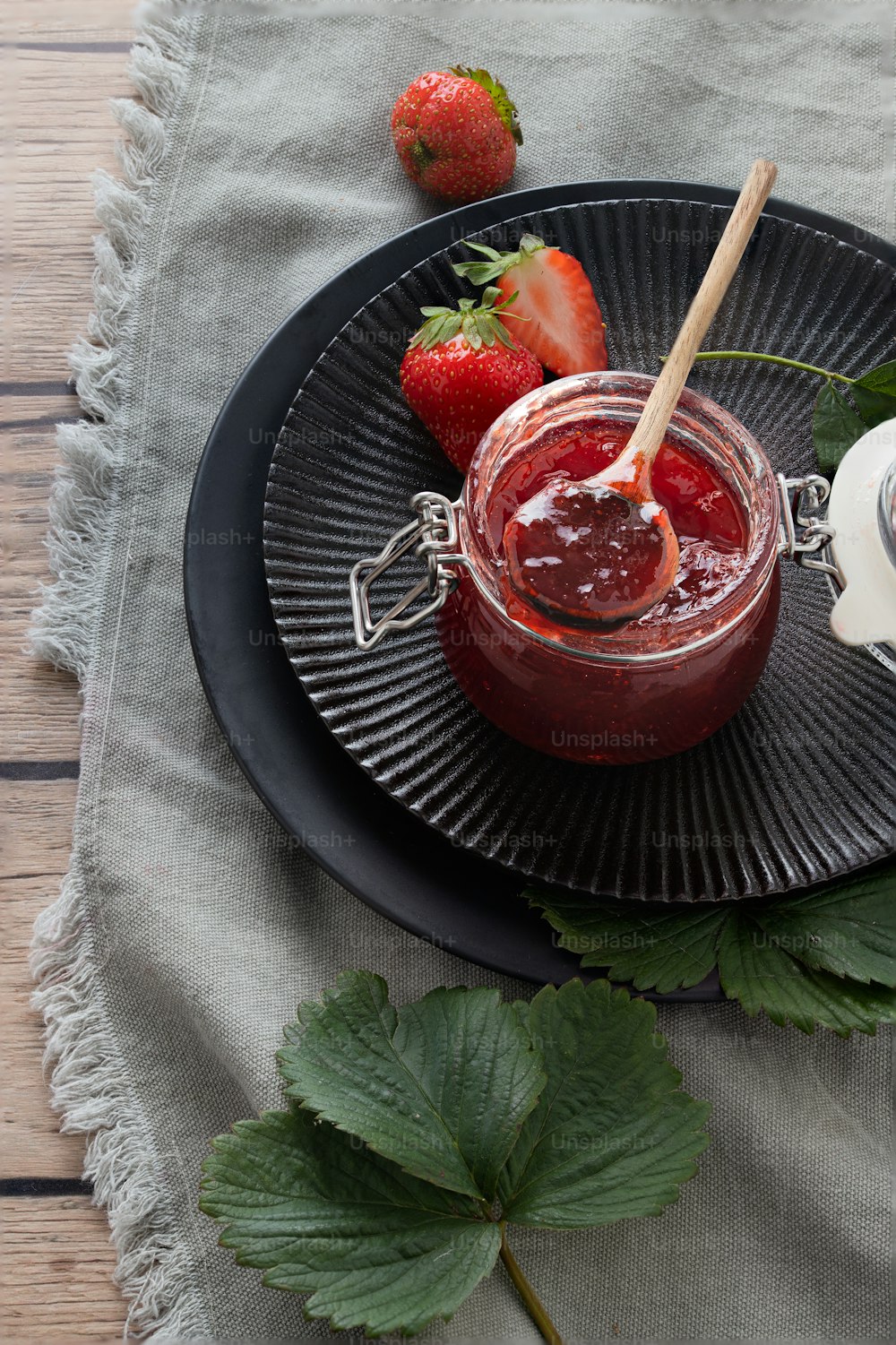 a plate with a jar of strawberry jam and two strawberries